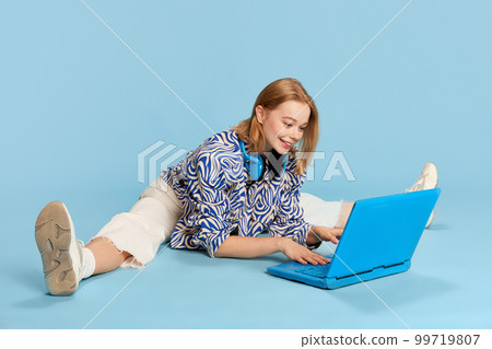 Happy smiling beautiful young girl, student working, studying and communicating on laptop over blue studio background 99719807