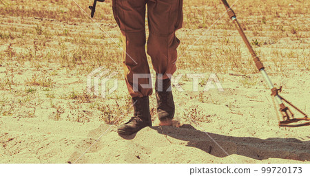 Soviet Army Sapper combat engineer deminer with a mine detector in his hands is looking for mines on the field. Bomb tech Bomb Squad In Historical Re-enactment of Soviet - Afghan War. Soviet Army Sapper combat engineer deminer with a mine detector in his hands is looking for mines on the field. Bomb tech Bomb Squad In Historical Re-enactment of Soviet - Afghan War. 99720173