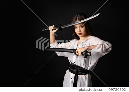 Asian woman wearing white kimono holding katana sword on a black background with copy space. 99720802