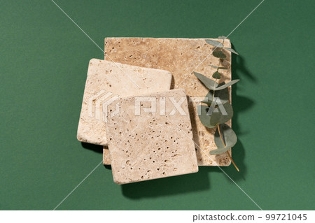 Travertine tile. Minimal composition, empty mockup template for product presentation made with natural travertine and eucalyptus on a dark green background. Flat lay with copy space. Top view. Travertine tile. Minimal composition, empty mockup template for product presentation made with natural travertine and eucalyptus on a dark green background. Flat lay with copy space. Top view. 99721045