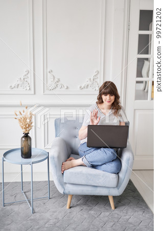 Woman waving hand has video call laptop computer online sitting in armchair at home. Hello there. Pleasant young female teacher or tutor sitting at home in cozy room before laptop Woman waving hand has video call laptop computer online sitting in armchair at home. Hello there. Pleasant young female teacher or tutor sitting at home in cozy room before laptop 99721202
