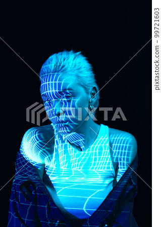 Abstraction and illusion. Portrait of young blonde girl with neon stripes on face posing over dark background in blue neon lights. Cyberpunk style 99721603