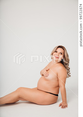a naked pregnant against the background of a white cyclorama in a photo studio. a naked pregnant against the background of a white cyclorama in a photo studio. 99722874