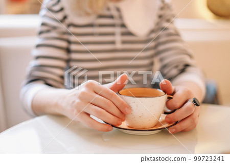 Woman with cup of coffee at white table table. Girl is holding coffee mug in hands. Woman with cup of coffee at white table table. Girl is holding coffee mug in hands. 99723241