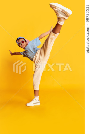 Dynamic portrait of little african boy, hip-hop dancer in stylish street style clothes dancing over bright yellow background. Concept of music, dance happiness Dynamic portrait of little african boy, hip-hop dancer in stylish street style clothes dancing over bright yellow background. Concept of music, dance happiness 99723532
