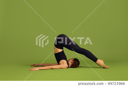 Strong fit body. Young flexible slim girl doing stretching and yoga exercises over green studio background. Concept of sport, body care, beauty Strong fit body. Young flexible slim girl doing stretching and yoga exercises over green studio background. Concept of sport, body care, beauty 99723966