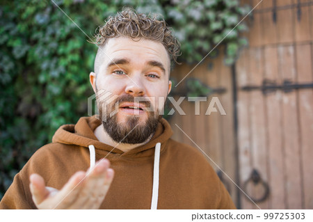 Young attractive vlog hipster and trendy style looking man smiling happy talking to camera posing cool with attitude dressing informal in selfie and internet video blogger recording 99725303