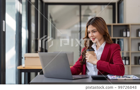 Asian business woman holding a cup of coffee at the desk Financial graph with desktop and laptop calculator for office marketing ideas Asian business woman holding a cup of coffee at the desk Financial graph with desktop and laptop calculator for office marketing ideas 99726848