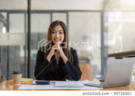 Asian Business woman using calculator and laptop for doing math finance on an office desk, tax, report, accounting, statistics, and analytical research concept 99726862