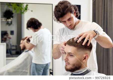 Barber trim hair with clipper on handsome bearded man Barber trim hair with clipper on handsome bearded man 99726928