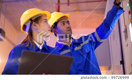 Professional electrical engineer team using laptop computer to inspecting the electrical circuit in control room. Team of electrical engineers having a discussion together about system maintenance. 99726999