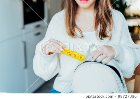 Woman putting daily pills organizer into her bag. Taking daily medicine antioxidant diet vitamin supplements for beauty skin hair health care medicament biohacking concept. Selective focus 99727386