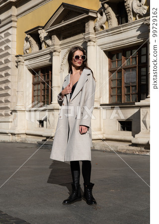 Street style, autumn, spring fashion concept: fashionable woman wearing luxury beige coat, sunglasses, wide leg black leggings, ankle bots, walking in street 99729162