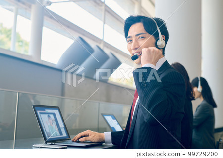 A businessman in a suit wearing a headset and responding in the office A businessman in a suit wearing a headset and responding in the office 99729200