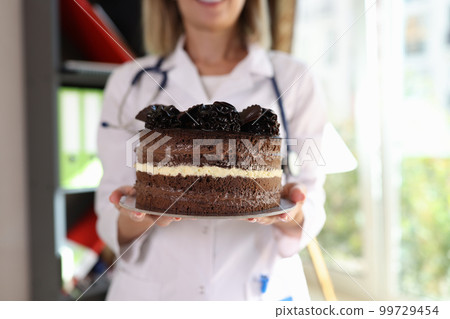 Female nutritionist holding large chocolate cake in hands 99729454