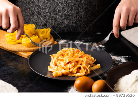 A close-up of hands holding a fork, digging into a plate of fast food in a kitchen. 99729520