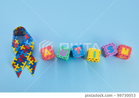 Word Autism Awareness day. Autism Awareness Ribbon and Puzzle cubes on blue background. Word Autism Awareness day. Autism Awareness Ribbon and Puzzle cubes on blue background. 99730053