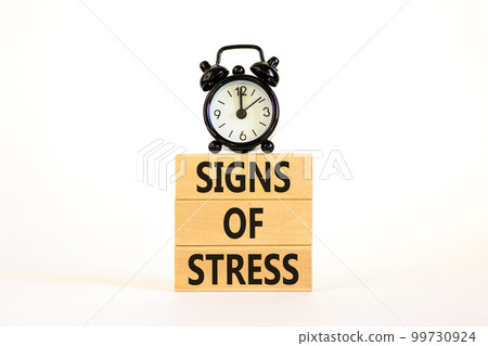 Signs of stress symbol. Concept words Signs of stress on wooden blocks. Black alarm clock. Beautiful white table white background. Psychological business and signs of stress concept. Copy space. 99730924