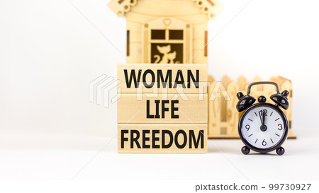 Woman life freedom symbol. Concept words Woman Life Freedom on wooden blocks on a beautiful white background. Black alarm clock, house model. Social issue woman life freedom concept. Copy space. 99730927