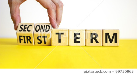First or second term symbol. Businessman turns wooden cubes, changes words first term to second term. Beautiful yellow table, white background. Business and first or second term concept, copy space. 99730962