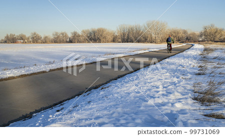 male cyclist commuting on a bike trail in winter scenery - Poudre River Trail in northern Colorado between WIndsor and Greeley 99731069