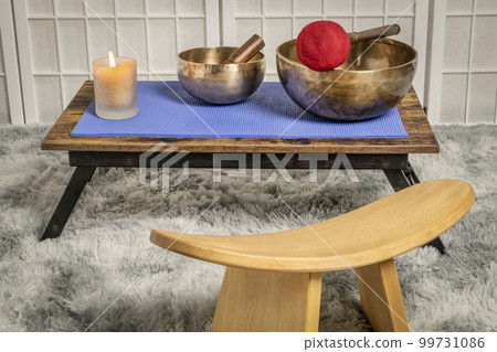 large Tibetan singing bowl with a mallet, roller and wax candle on a low table, and kneeling bench, sound healing and meditation concept 99731086