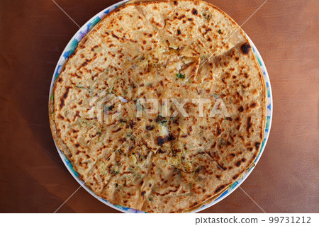 Potato stuffed paratha, aloo vali roti, torn in the middle for the filling visibility, top view.  A round oriental flatbread stuffed with potato, onion, herbs, spices, popular in the Punjab. Close-up. 99731212