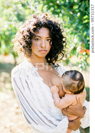 Woman in white dress breastfeeding her newborn baby in the garden Woman in white dress breastfeeding her newborn baby in the garden 99731357