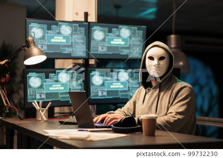 Hacker wearing mask and hood to hack computer system, breaking into company servers to steal big data. Masked man looking dangerous and scary, impostor creating security malware. Hacker wearing mask and hood to hack computer system, breaking into company servers to steal big data. Masked man looking dangerous and scary, impostor creating security malware. 99732230