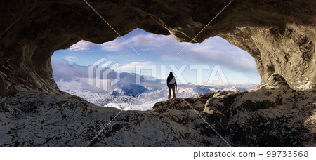 Adventurous Man Hiker standing in an Ice Cave with rocky mountains in background. Adventure Composite 99733568