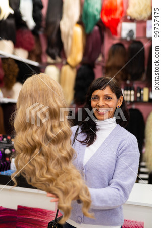 Hispanic woman choosing natural hair wigs in speciality store Hispanic woman choosing natural hair wigs in speciality store 99737475