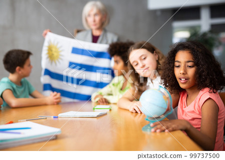Female teacher showing uruguayan flag to kids in geography class Female teacher showing uruguayan flag to kids in geography class 99737500