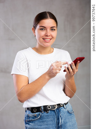 Cheery young woman holding mobile phone Cheery young woman holding mobile phone 99737641