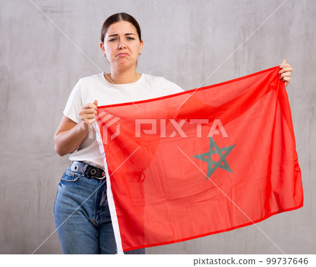Stressed out sad young woman standing with flag of Morocco against gray wall Stressed out sad young woman standing with flag of Morocco against gray wall 99737646