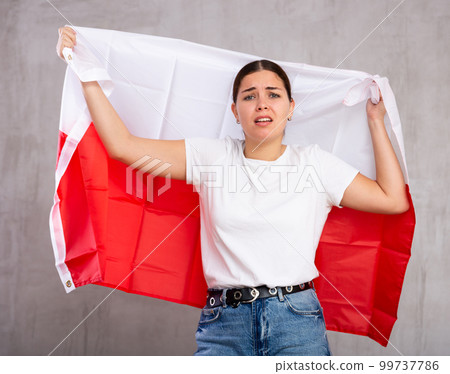 Sad young woman holding Poland flag against unicoloured background Sad young woman holding Poland flag against unicoloured background 99737786