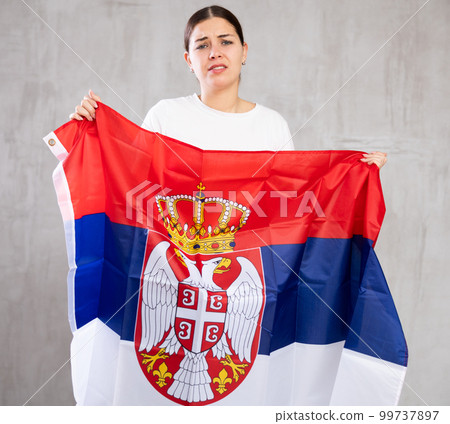 Irritated girl stands with flag of Serbia. Isolated on gray background Irritated girl stands with flag of Serbia. Isolated on gray background 99737897