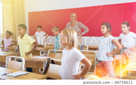 Preteen schoolchildren with teacher performing physical exercises in classroom Preteen schoolchildren with teacher performing physical exercises in classroom 99738011