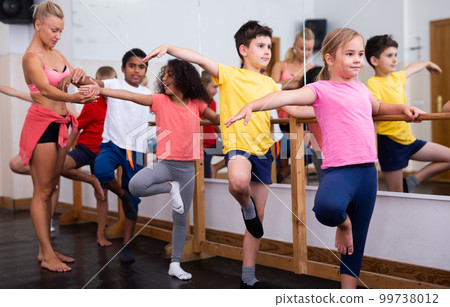Preteen girl practicing dance movements with group of children Preteen girl practicing dance movements with group of children 99738012