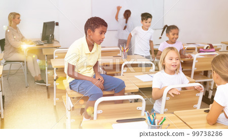 Positive primary school students are talking about homework at desk Positive primary school students are talking about homework at desk 99738286