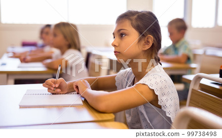 Focused tween schoolgirl writing in workbook during lesson Focused tween schoolgirl writing in workbook during lesson 99738498