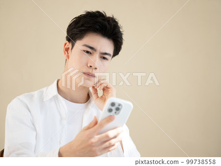 一個表情嚴肅的年輕帥哥拿著智能手機特寫 99738558
