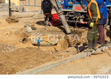 Workers use a suction excavator based on a truck to sample soil in a well for communications 99742019