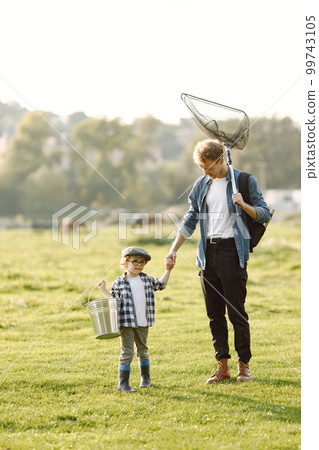 Dad and his child boy spend time outdoors together. Curly toddler boy wearing a plaid shirt and a hat. Boy holding a hand of his father. Dad and his child boy spend time outdoors together. Curly toddler boy wearing a plaid shirt and a hat. Boy holding a hand of his father. 99743105