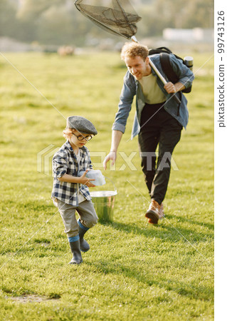 Dad and his child boy spend time outdoors together. Curly toddler boy wearing a plaid shirt and a hat. Boy holding a hand of his father. Dad and his child boy spend time outdoors together. Curly toddler boy wearing a plaid shirt and a hat. Boy holding a hand of his father. 99743126