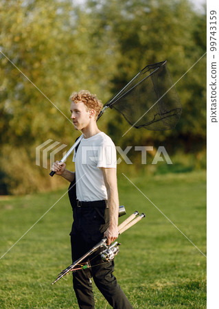 Fisherman is ready to go fishing. Blonde man holding a fishing equipment. Man wearing white t-shirt and black trousers. 99743159