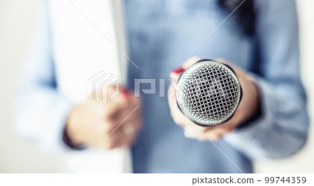Female journalist at a press conference with a microphone and notebook Female journalist at a press conference with a microphone and notebook 99744359