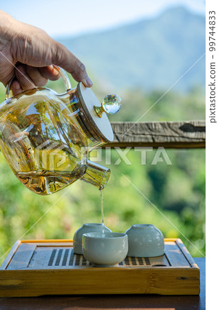 male hand is holding teapot and pouring tea into teacup with green background male hand is holding teapot and pouring tea into teacup with green background 99744833