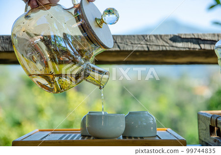 male hand is holding teapot and pouring tea into teacup with green background male hand is holding teapot and pouring tea into teacup with green background 99744835