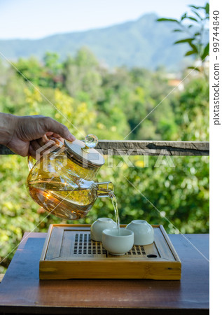 male hand is holding teapot and pouring tea into teacup with green background male hand is holding teapot and pouring tea into teacup with green background 99744840