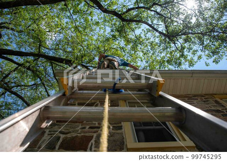 Low angle view of man on ladder cleaning gutters of stone home Low angle view of man on ladder cleaning gutters of stone home 99745295